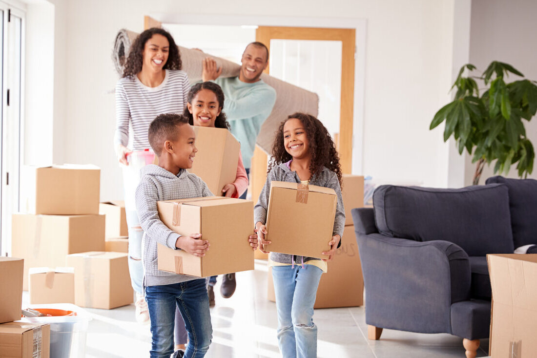 A family carrying moving boxes into their new home, all smiling